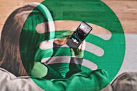 a woman is sitting on a couch with a spotify logo on her phone